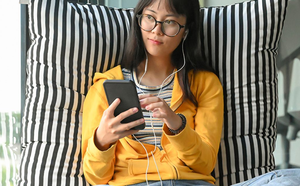 Young woman holding smartphone with headphones attached.