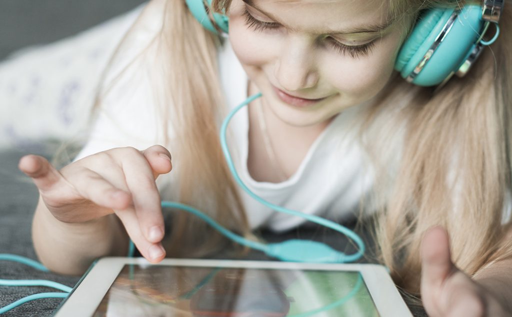 young girl playing on tablet with headphones on.