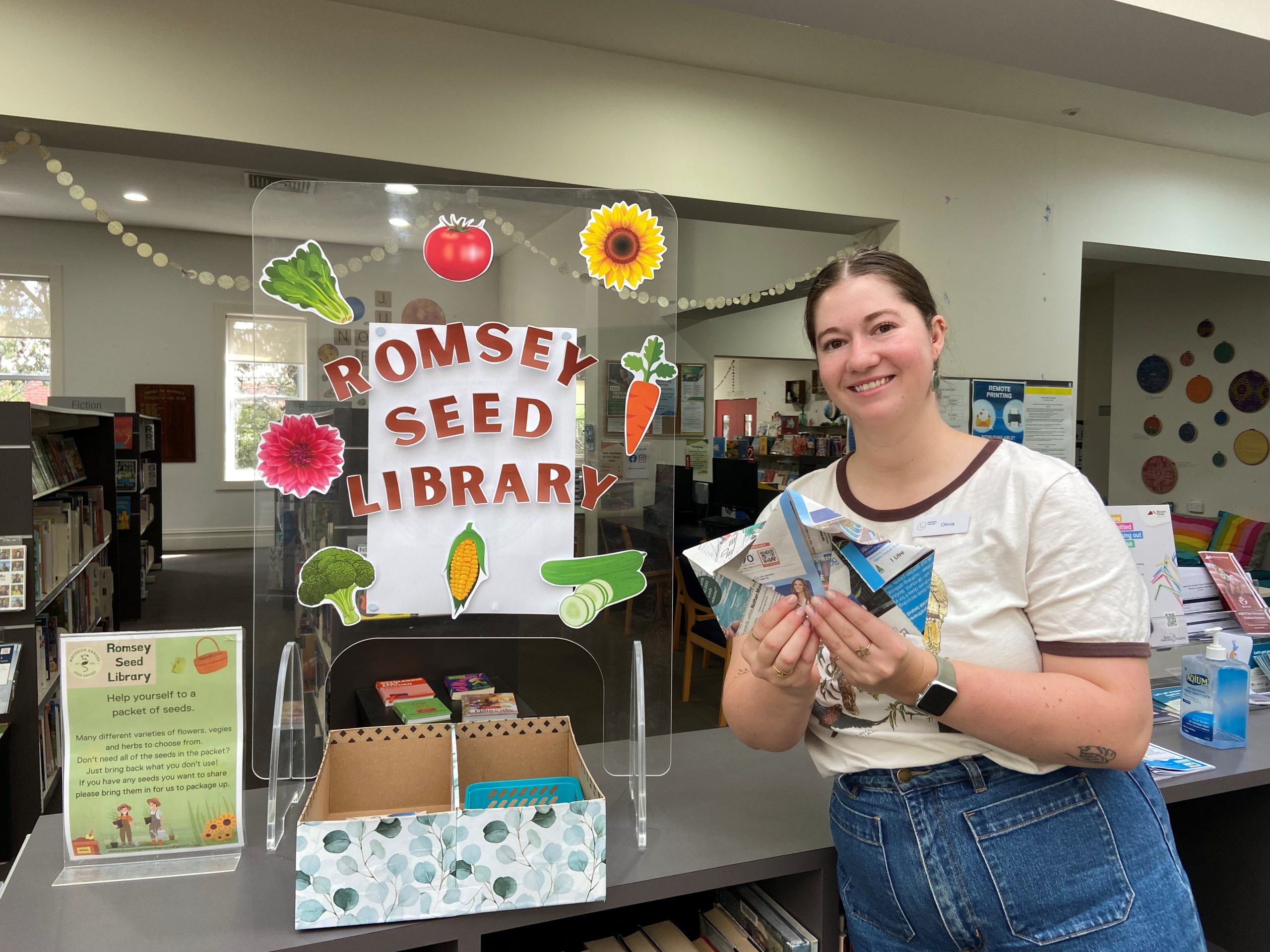 Woman holding seed packets, standing in front of the Romsey Seed Library.