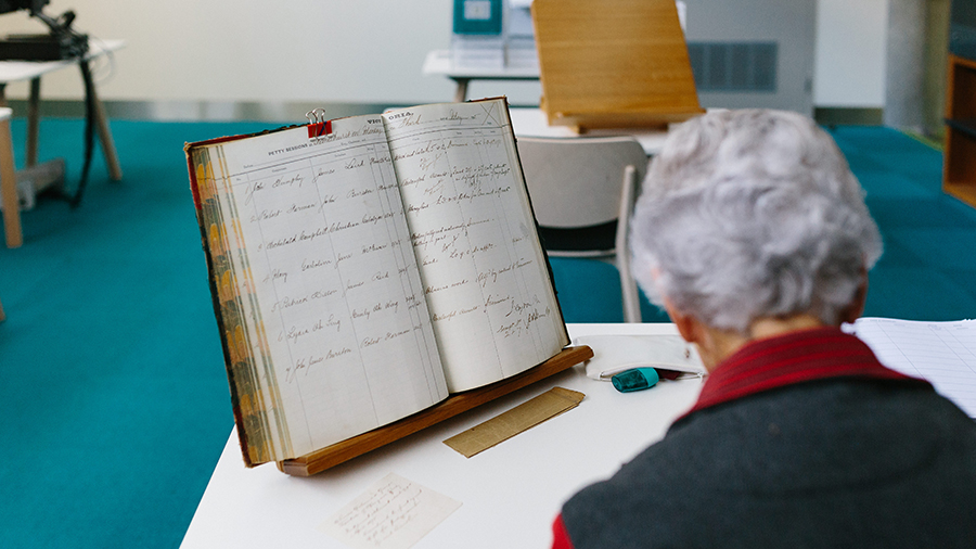 senior woman transcribes an old rate book.