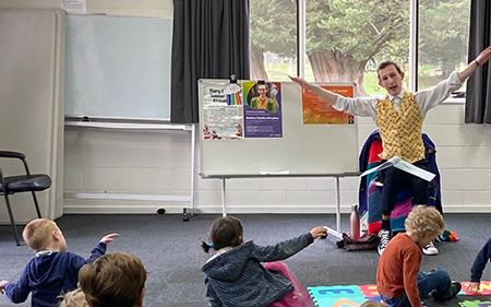 Em Chandler in a yellow vest and vest leads children in a fun Rainbow Families storytime session at Woodend Library.