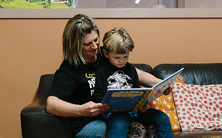 A woman and a child sit on a couch at Castlemaine Library, reading a book together.