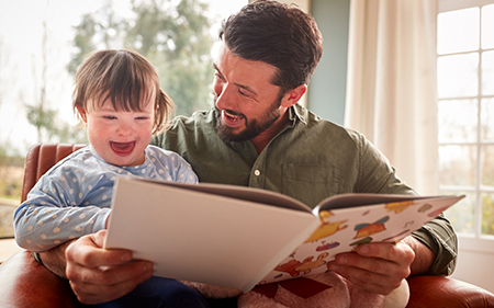 A man and a little girl sit together, happily reading a book, sharing smiles and enjoying their time together.