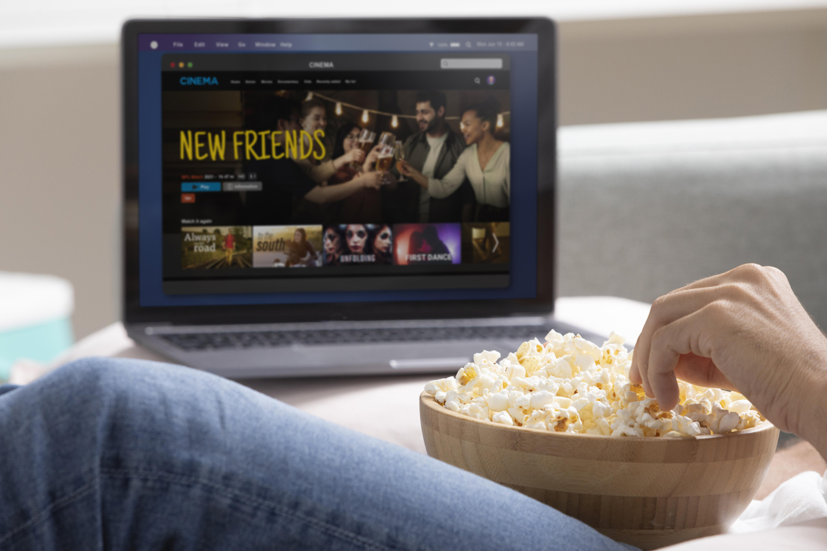 laptop with a streaming service showing. In the foreground is a person's hand in a bowl of popcorn.